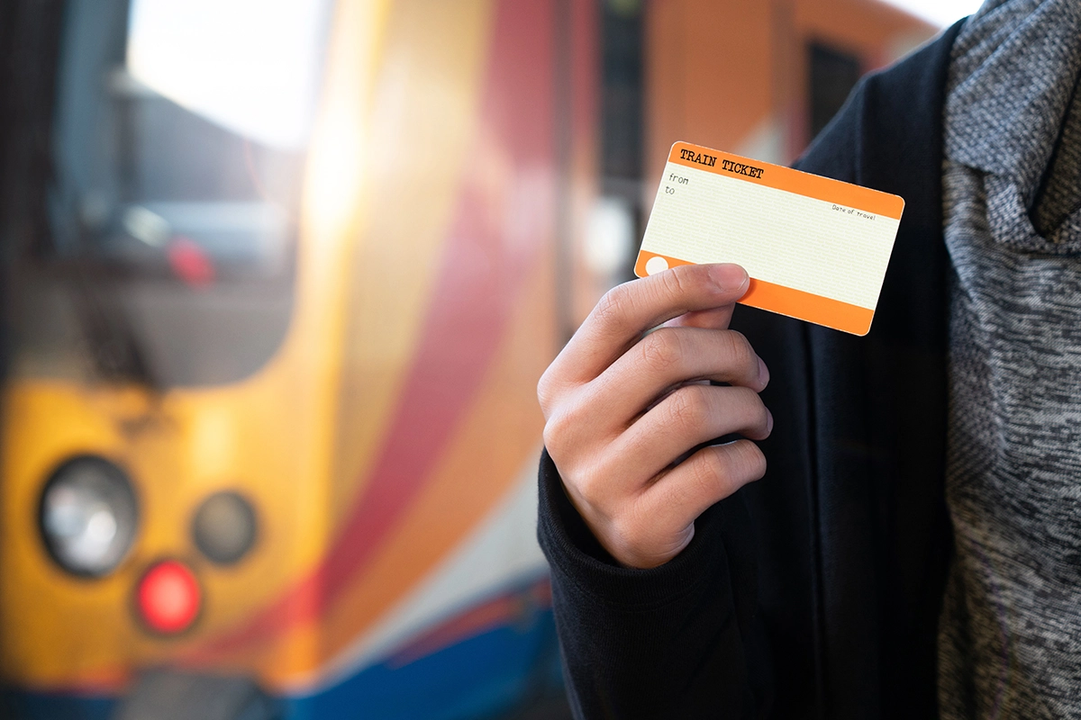 Person holding train ticket in front of train