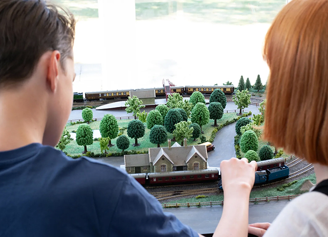 Man and woman moving their Hornby train onto the tracks of their model railway. 