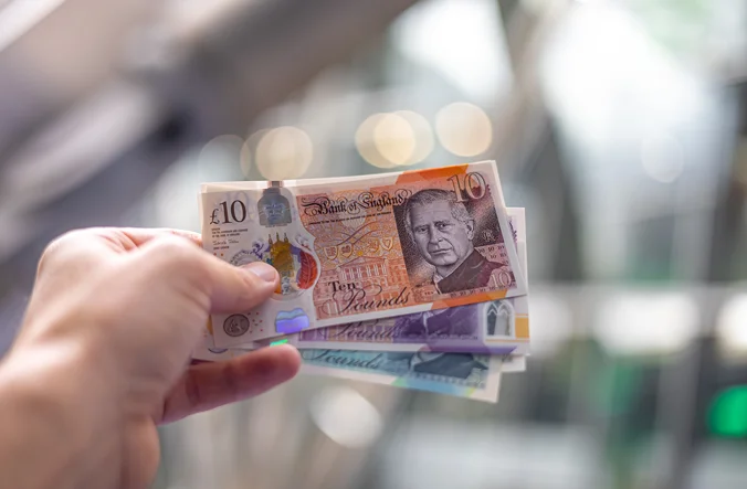 Hand holding several notes showing King Charles.