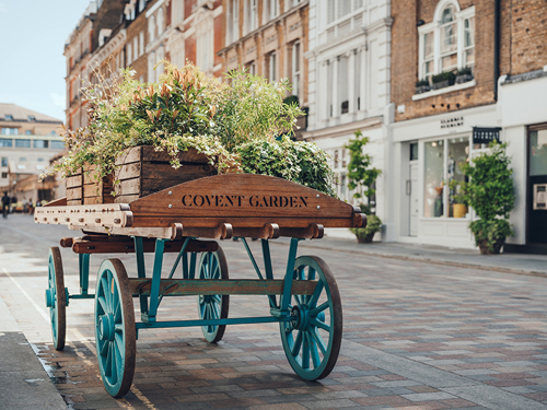 'Covent Garden" area name sign on a wooden cart with flowers on a street in Covent Garden, London, UK, on a bright summer day.