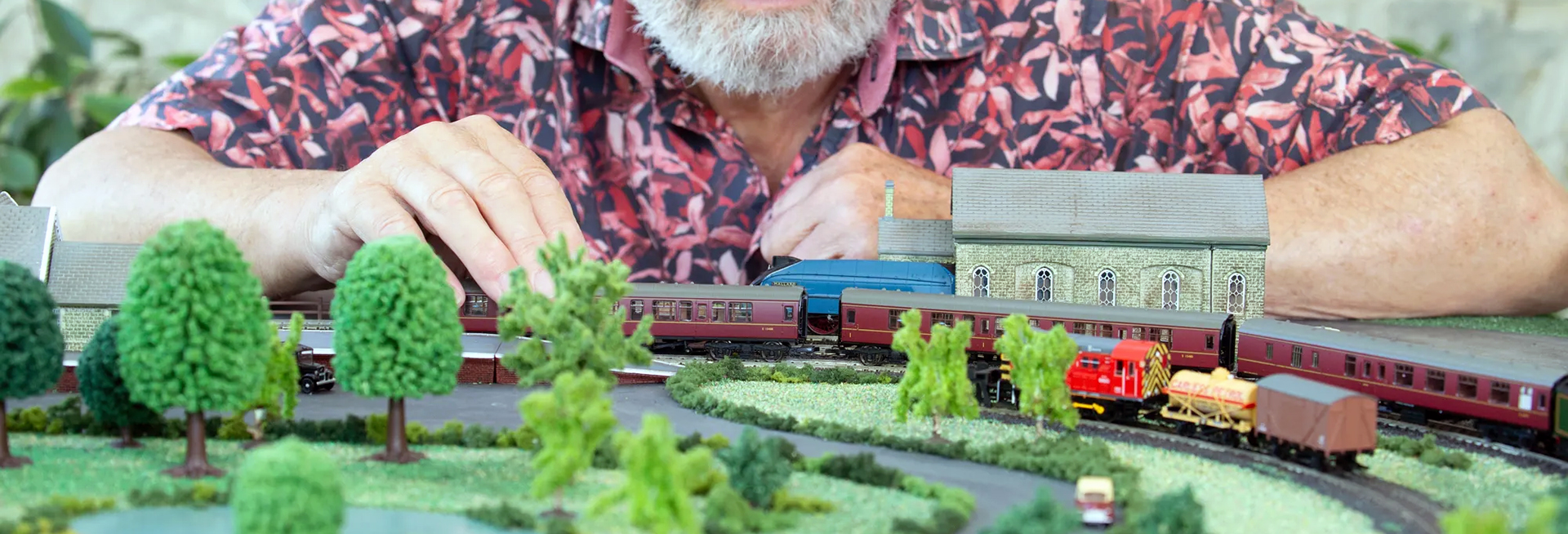 Man in colourful shirt with a model railway. 